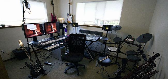 Một người đang thu âm bài hát bằng microphone và laptop trong phòng thu nhỏ tại nhà.